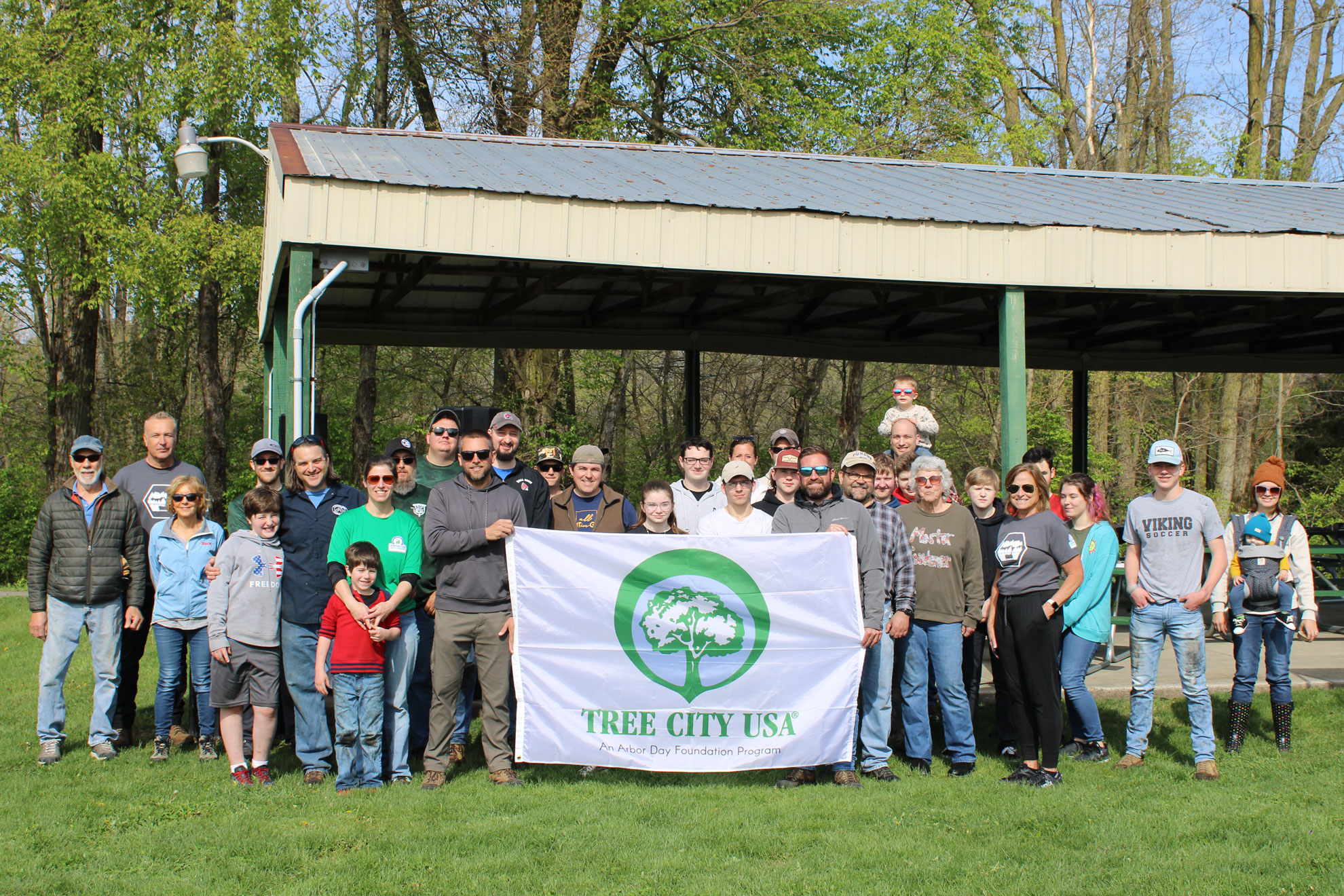 A large group of volunteers hold a banner with the words Tree City USA