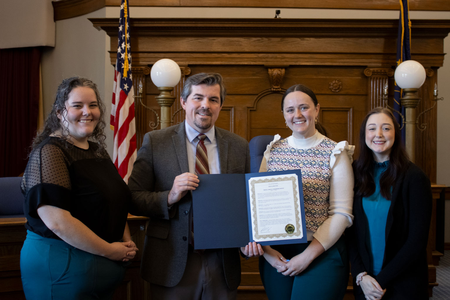 A mayor presents three women with a signed proclamation