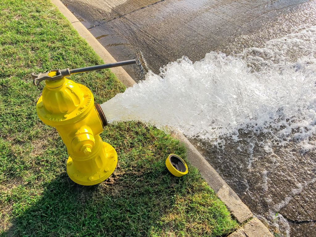 Water being flushed from a yellow fire hydrant onto a paved surface
