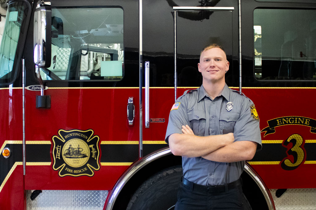Firefighter in uniform standing beside a firetruck.