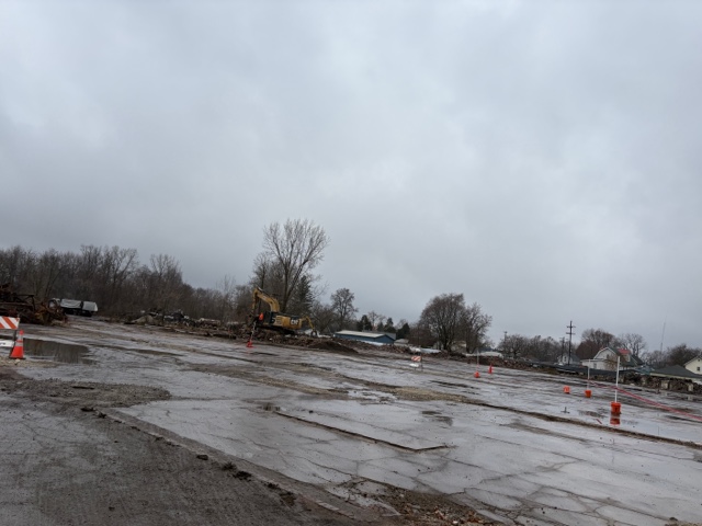 An excavator clears debris at the H.K. Porter site after the building has been fully demolished, with piles of concrete and steel visible in the background.