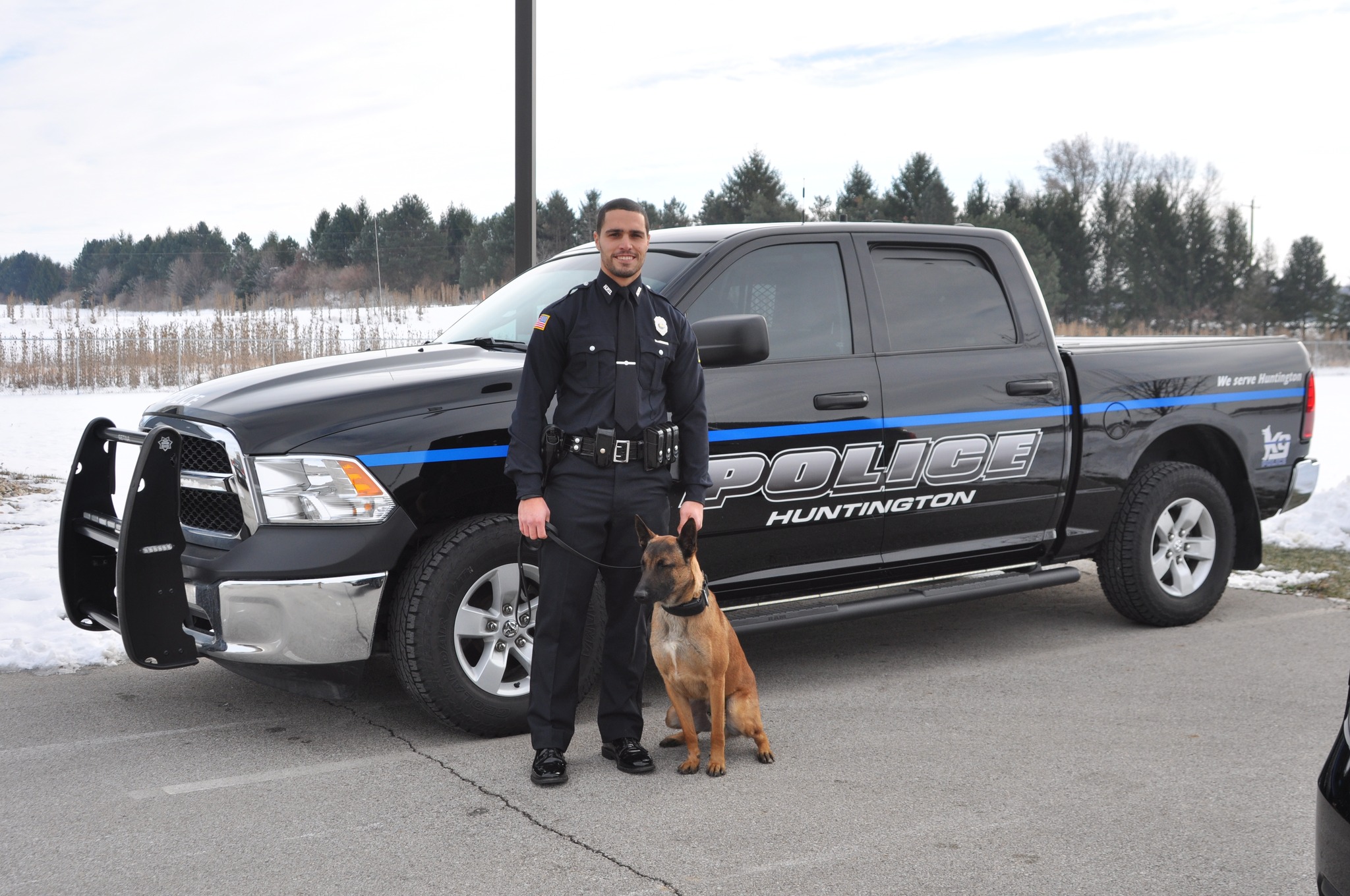 A police officer and police canine stand in front of a Huntington Police Department truck.