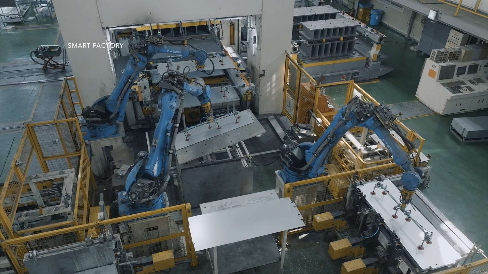 Overhead view of industrial production equipment inside a Hanjung facility, with blue robotic arms moving large metal panels in a clean factory space.